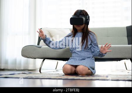 Ein süßes und aufgeregtes junges asiatisches Mädchen trägt ein VR-Headset und erlebt zu Hause ein Virtual-Reality-Spiel. Virtual-Reality-Gaming Stockfoto