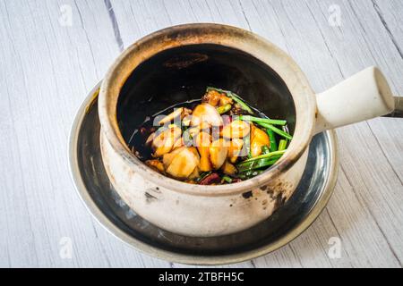 Froschkeule mit Frühlingszwiebeln und getrockneten Schilf-Chili unter Rühren anbraten und in einem Tontopf serviert Stockfoto