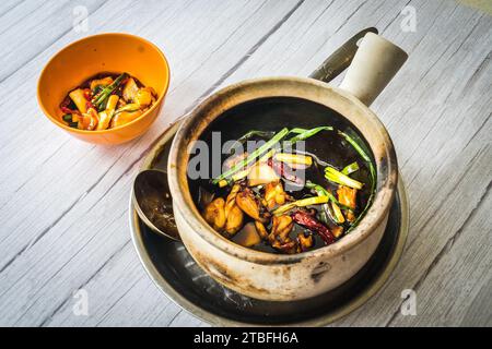 Froschkeule mit Frühlingszwiebeln und getrockneten Schilf-Chili unter Rühren anbraten und in einem Tontopf serviert Stockfoto