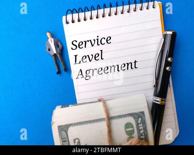 Banknoten, Stift und Notizbuch mit Text Service Level Agreement auf blauem Hintergrund. Stockfoto