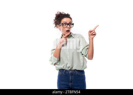 Junge überraschte brünette Frau mit Brille zeigt mit ihren Händen auf weißem Hintergrund im Kopierraum Stockfoto
