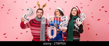 Gruppe glücklicher männlicher und weiblicher Freunde, die Pullover tragen, die Weihnachten 2023 feiern, Studio-Porträt in rosa Farbe Banner Hintergrund Stockfoto