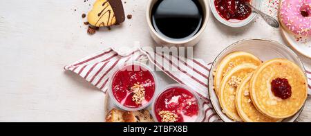 Tisch mit verschiedenen amerikanischen Keksen, Donuts, Pfannkuchen und Kaffeetassen auf weißem Hintergrund. Draufsicht. Panorama mit Kopierbereich. Stockfoto