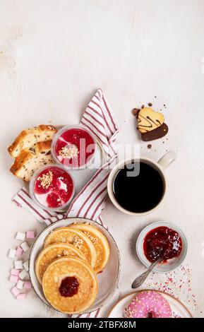 Tisch mit verschiedenen amerikanischen Keksen, Donuts, Pfannkuchen und Kaffeetassen auf weißem Hintergrund. Draufsicht. Kopierbereich. Stockfoto