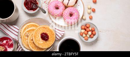 Tisch mit verschiedenen amerikanischen Keksen, Donuts, Pfannkuchen und Kaffeetassen auf weißem Hintergrund. Draufsicht. Panorama mit Kopierbereich. Stockfoto