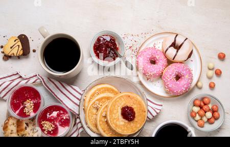Tisch mit verschiedenen amerikanischen Keksen, Donuts, Pfannkuchen und Kaffeetassen auf weißem Hintergrund. Draufsicht. Kopierbereich. Stockfoto