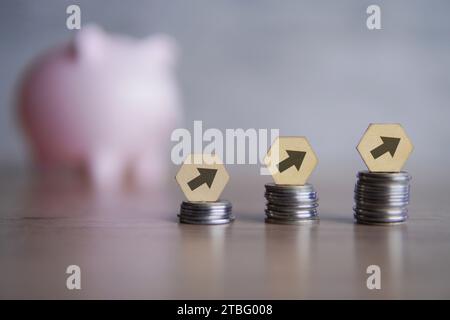 Ein Stapel Münzen mit Pfeilen, die nach oben zeigen, vor einer Schweinebank. Finanzwachstum, Sparen von Geld. Stockfoto