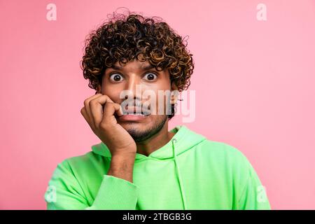Porträt eines lustigen unglücklichen indischen Studenten, der sich vor der Abschlussprüfung in der Universität in die Nägel beißt, isoliert auf rosafarbenem Hintergrund Stockfoto