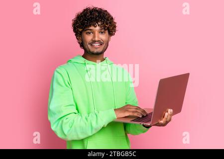 Foto des fröhlichen jungen Mannes indianer Guy lockige Haare Studenten studieren mit Netbook online während Pandemie isoliert auf rosa Hintergrund Stockfoto