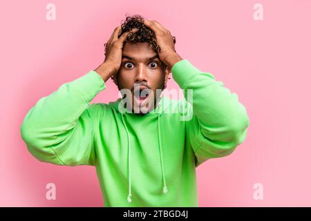 Porträt des sprachlosen lustigen jungen indianers grünes Sweatshirt verwirrte Hände berühren Kopf schockiert starren isoliert auf rosa Hintergrund Stockfoto
