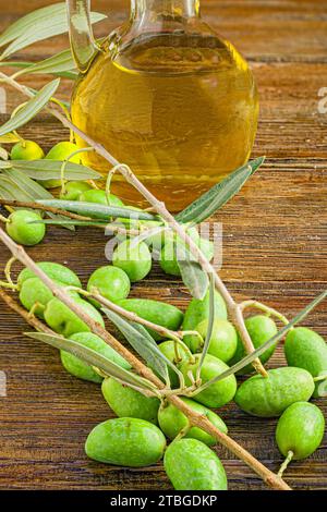 Ein Glaskrug mit Olivenöl und ein paar verstreute Oliven um den Tisch Stockfoto