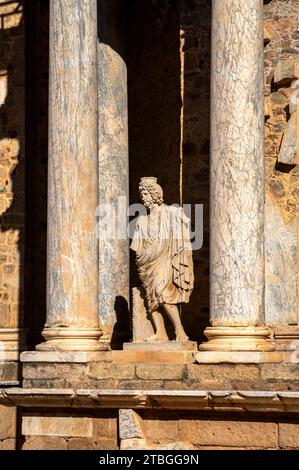 Ruinen einer klassischen Statue mit Toga und griechischen und römischen Säulen des römischen Theaters von Mérida in Extremadura, beleuchtet durch den Kontrast der Dämmerung LIG Stockfoto