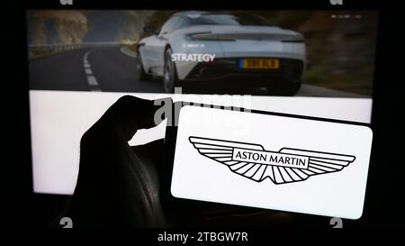 Person mit Smartphone und Logo des britischen Unternehmens Aston Martin Lagonda Global Holdings plc vor der Website. Schwerpunkt auf dem Display des Telefons. Stockfoto