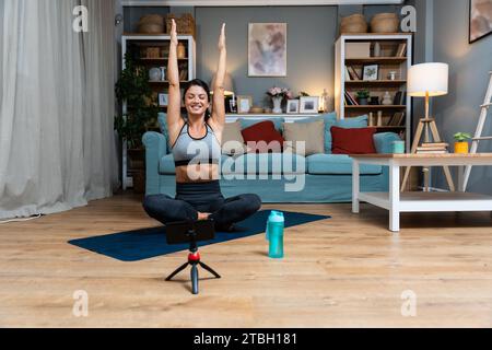 Attraktive junge Frau lernt neue Übungen und sieht sich Online-Trainings über ihr Telefon zu Hause an. Hübsche Frau, die Yoga-Klasse übt, mit V Stockfoto