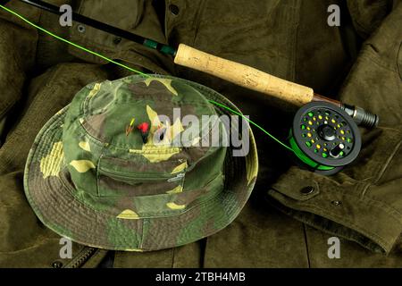 Fliegenfischrute und -Rolle mit Fliegenleine auf einem Außenmantel mit Forellenfliegen auf einem Angelhut Stockfoto