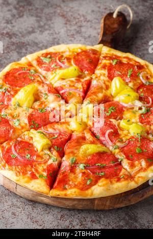 Scharfe Salami-Pizza mit Paprika, roten Zwiebeln, Mozzarella und Kräutern aus nächster Nähe auf einem Holzbrett auf dem Tisch. Vertikal Stockfoto