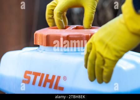 Die Hände des Gärtners in Schutzhandschuhen verschließen den Deckel des Tanks mit Kupfersulfat aus einer Stihl Gartenspritze Stockfoto