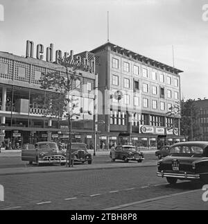 1955 ein Straßenblick von Rotterdam – fotografiert mit Blick über Beursplein in der Nähe der Kreuzung mit Coolsingel (rechts). Die geparkten Autos gehören der Vergangenheit an, Beursplein ist heute mit einem Einkaufszentrum und einer U-Bahn-Station unter dem Boden zu Fuß erreichbar. An der Ecke befindet sich ein C&A Bekleidungsgeschäft (heute stark modernisiert). Neonschilder an einem Gebäude zeigen „Nederland“ und „Kattenburg“ (eine Regenbekleidungsmarke) – ein Vintage-Foto aus den 1950er Jahren. Stockfoto