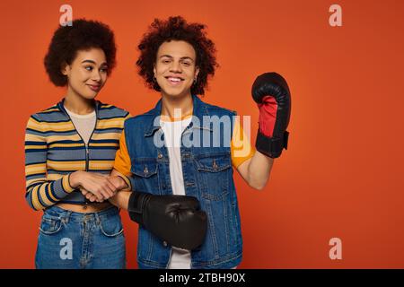 Fröhlicher afroamerikanischer Mann in Boxhandschuhen, der Spaß mit seiner Schwester vor orangefarbenem Hintergrund hat, Familie Stockfoto