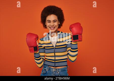 Schöne fröhliche afroamerikanische Frau posiert aktiv mit Boxhandschuhen auf orangefarbenem Hintergrund Stockfoto