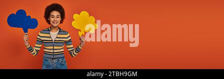 Hübsche afroamerikanerin posiert mit blauen und gelben Gedankenblasen auf orangefarbenem Hintergrund, Banner Stockfoto