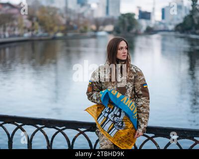 Ukrainische Soldatenfrau mit Flagge und Unterschriften ukrainischer Krieger und ruht im Park im Urlaub. Übersetzung aus dem Ukrainischen: Bewaffnete Kräfte o Stockfoto