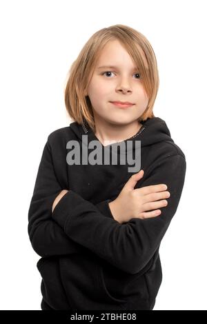 Ein kleiner Junge mit langen Haaren steht selbstbewusst, Arme auf der Brust gekreuzt, in einem ausgewogenen Porträt vor einem sauberen weißen Hintergrund. Stockfoto