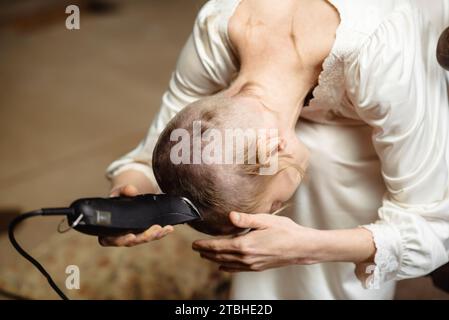 Der Hinterkopf ist eine Frau, die ihr eigenes Haar auf dem Kopf schneidet. Sich selbst der Haare berauben. Herausforderung an die Gesellschaft. Stockfoto