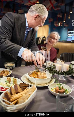 Senior-Mann, der gebratenes Huhn zum Weihnachtsessen mit Frau im Restaurant schneidet Stockfoto