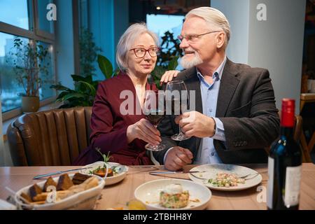 Niedliches Age-Paar, das Weingläser anklickt, um Weihnachten zusammen zu feiern Stockfoto