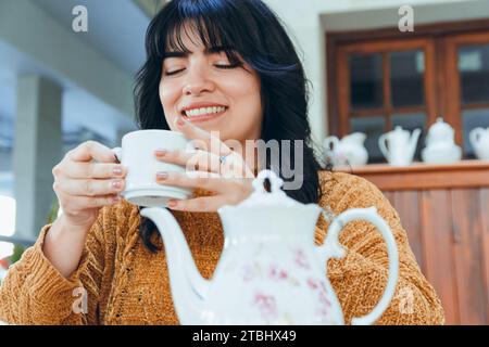 Junge schwarzhaarige venezolanische Frau glücklich lächelnd sitzt im Restaurant und genießt den Tag bei einer Tasse Tee Stockfoto