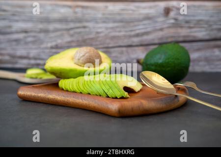 Halbierte und fein geschnittene Avocado auf Holzplatte auf schwarzem Hintergrund. Stockfoto