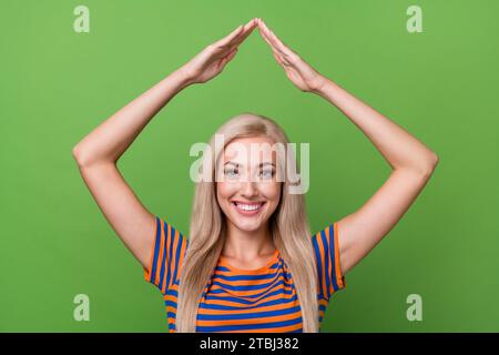 Foto des fröhlichen hübschen Mädchens tragen stilvolle Kleidung zwei Hände über Kopf kaufen Wohnhaus Hütte isoliert auf grünem Farbhintergrund Stockfoto