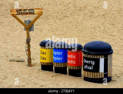 Vier Mülltonnen, um den Abfall am Strand zu trennen. Sie sind auf Niederländisch gekennzeichnet: Glas, Papier, Kunststoff, andere Abfälle. Auf dem Pol steht: Wirf es her, sa Stockfoto