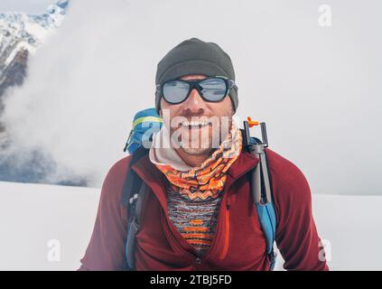 Fröhlicher, lachender Kletterer im Sonnenbrillen-Porträt mit Rucksack, der die hohen Hänge des Mera-Gipfels auf 6000 m Höhe ansteigt und bei schönem sonnigem Wetter, körperlichem Cha genießt Stockfoto