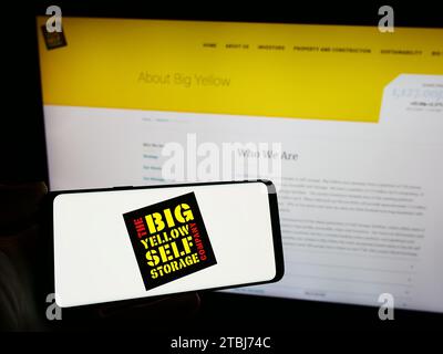 Person, die ein Smartphone mit dem Logo des britischen Selbstspeicherunternehmens Big Yellow Group plc vor der Website hält. Schwerpunkt auf dem Display des Telefons. Stockfoto