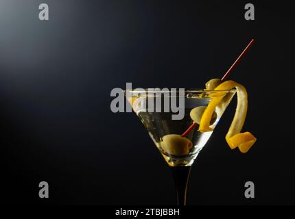 Glas klassischer trockener Martini-Cocktail mit grünen Oliven und Zitronenschale auf schwarzem Hintergrund. Freier Platz für Ihren Text. Stockfoto