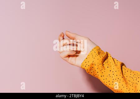 Leere weibliche Hand mit bemalten Nägeln in Gold glitzernder Farbe vor rosa Hintergrund, Maniküre Stockfoto