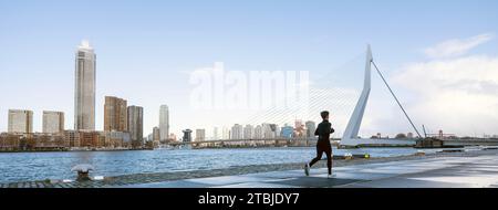 Frau joggt in der Nähe der erasmus-Brücke, gesehen vom Ufer von kop van zuid in der niederländischen Stadt rotterdam Stockfoto