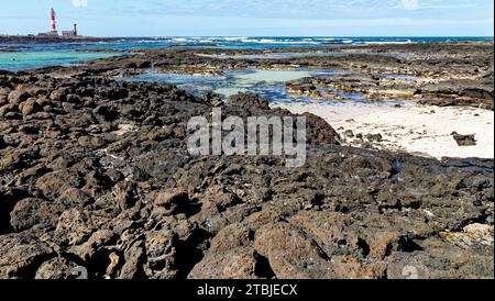 Natürliche Gezeitenbecken am Strand Playa de los Charcos und Leuchtturm von Toston - natürliche Pools am Strand von Los Laguitos oder Los Charcos auf Fuerteventura, Stockfoto