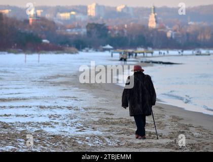 Ostsee Winter einsame Seniorin mit einem Stock, die an einem kalten Wintertag am schneebedeckten Danziger Strand entlang in Richtung der Kurstadt Sopot an der Ostseeküste, Polen, Europa, EU Stockfoto