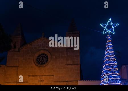 Weihnachtsbaum mit LED-Beleuchtung an der Fassade der Kirche der mallorquinischen Stadt Portocolom bei Nacht. Spanien Stockfoto