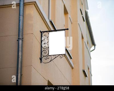 Leeres Vintage-Ladenschild an einem Gebäude. Leerer Kopierbereich zum Einfügen eines Logos oder der Öffnungszeiten. Stahlrahmen mit Ornamenten im Design montiert. Stockfoto