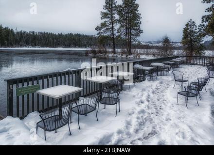 Dieses atemberaubende Bild zeigt einen schneebedeckten Balkon mit Tischen und Stühlen mit Blick auf einen wunderschönen Fluss Stockfoto