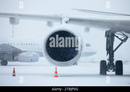 Verkehr am Flughafen bei starkem Schneefall. Schneeflocken gegen Düsentriebwerk und Rollflugzeug auf dem Rollweg des Flughafens an frostigen Wintertagen. Extremer Witterungseinfluss Stockfoto