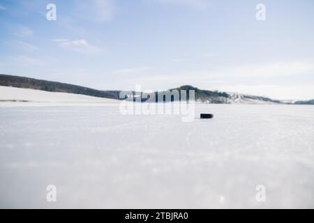 Eishockeypuck auf einem gefrorenen See im Winter vor dem Hintergrund der Berge. Stockfoto