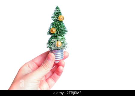 Hand, die einen verzierten Weihnachtsbaum hält, der in einer Glühbirnenbasis auf weißem Hintergrund platziert ist. Weihnachtsstimmung mit einem Hauch von Kreativität. Stockfoto