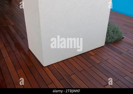 Moderne verputzte weiße Betonsäule auf Hartholzterrassenboden Terrasse Detail Idee, blauer Pool auf Hintergrund Stockfoto