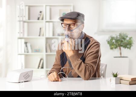 Ein älterer Mann sitzt auf einem Tisch und benutzt zu Hause einen Vernebler mit Dampfnebel Stockfoto