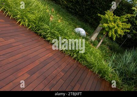 Hölzerne braune Terrassendielen ipe Textur und Gartengrün mit immergrünem Ziergras auf Hintergrund Stockfoto